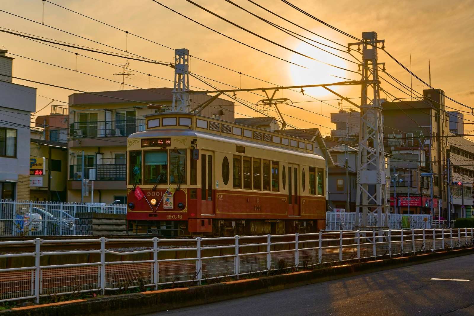 夕暮れ時のオレンジ色の空を背景に、川沿いの高架を走る都電荒川線