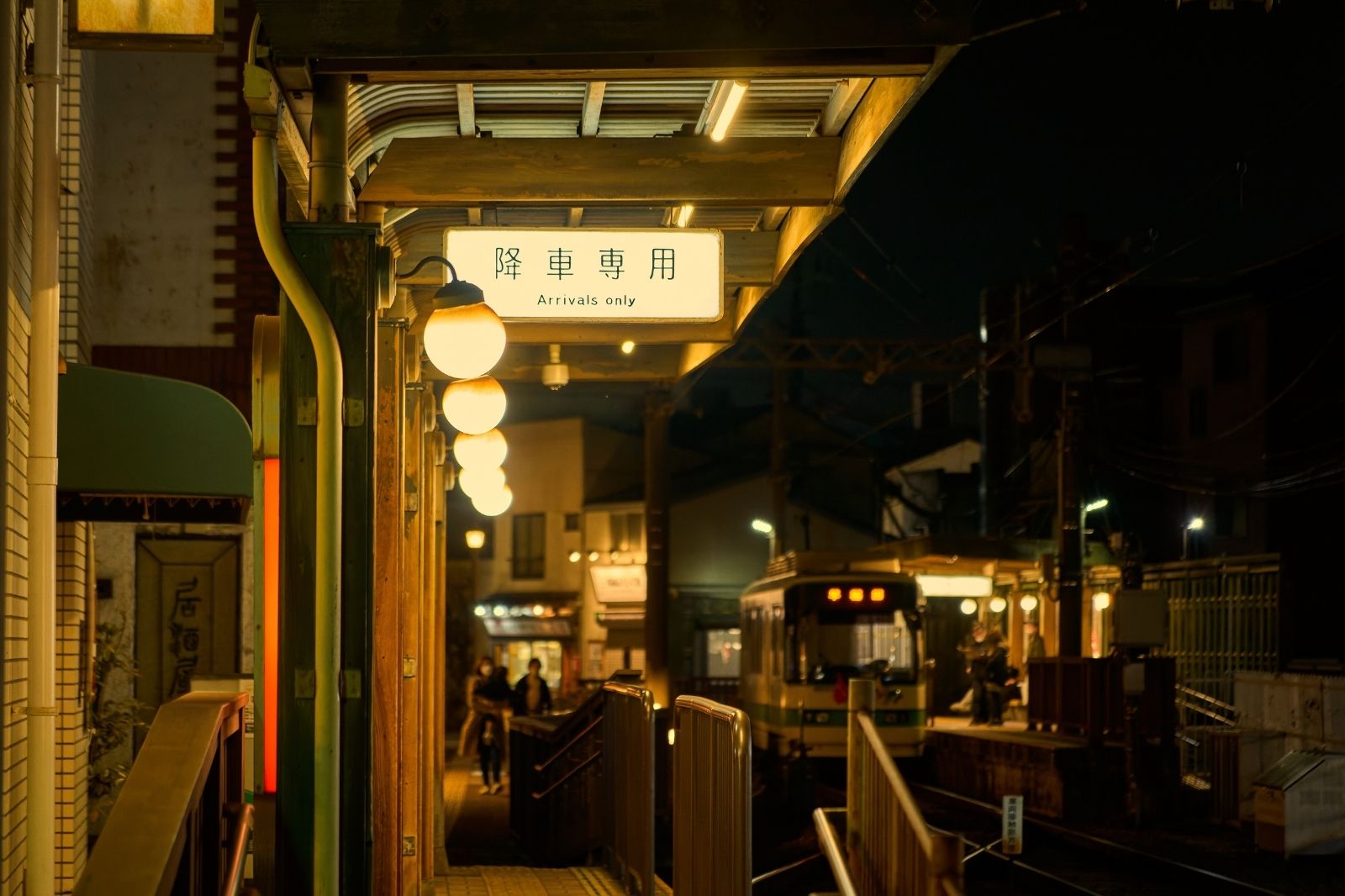 夜の電停。「降車専用 Arrivals only」の看板が灯る温かみのある風景